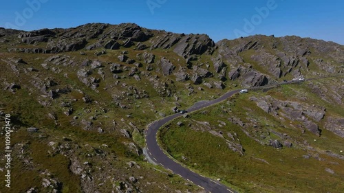 Healy Pass, County Cork, Ireland, September 2024. Drone ascends while following a car driving along single lane road towards the summit of the mountain bordering County Kerry under a clear blue sky. photo