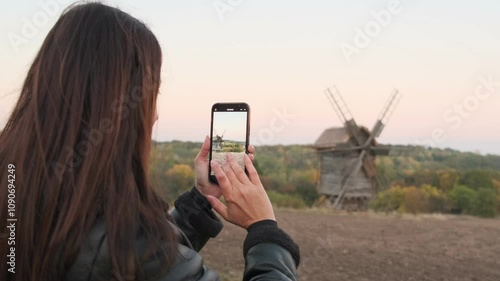 Female tourist adjusting zoom on smartphone to capture the best shot of a landscape with historical buildings.