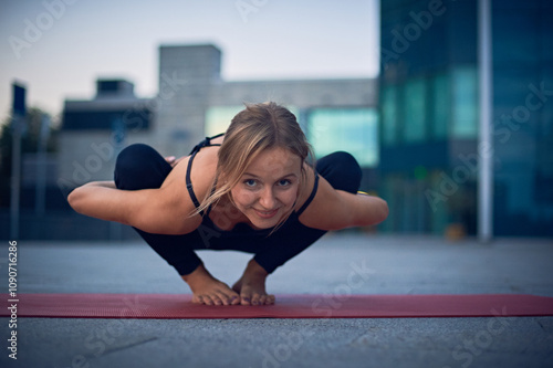 Yoga practitioner demonstrates advanced crow pose on a mat in an urban setting during sunset photo