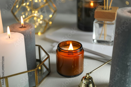 Beautiful burning candles on light table against blurred lights, closeup photo