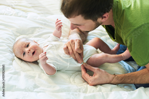 Father gently dressing his baby in a cozy bedroom during morning hours photo