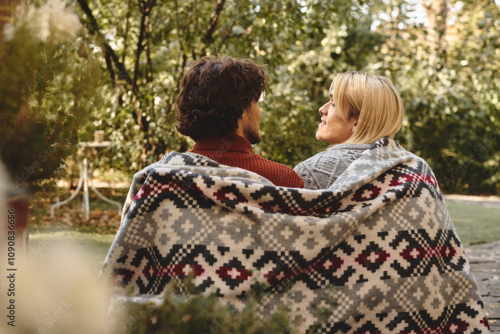 A young and handsome pair relax under a cozy blanket in a lush garden, enjoying each others company during a peaceful afternoon. A young and handsome pair relax under a cozy blanket in a lush garden, enjoying each others company during a peaceful afternoon.