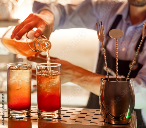 Bartender pouring juice into two glasses with ice on bar counter