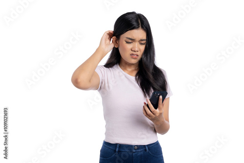 Confused young Asian woman looking at smartphone with a frustrated expression, scratching head while reading message isolated on white background photo