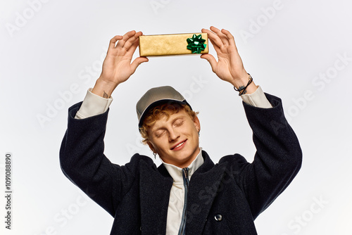 A cheerful man presents a beautifully wrapped gift, showcasing stylish holiday fashion. Dressed in a cozy coat and cap, he radiates excitement for the Christmas festivities in 2025.