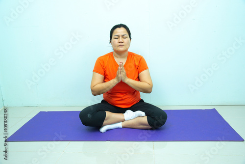 A woman practices yoga on a yoga mat in the comfort of his home. The individual is engaged in physical exercise within a well-lit room, emphasizing the importance of a healthy lifestyle.