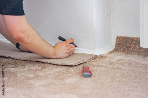 Male professional worker fitting carpet on floor after repair. Man handling carpet fitting and cutting, highlighting expertise in apartment renovation