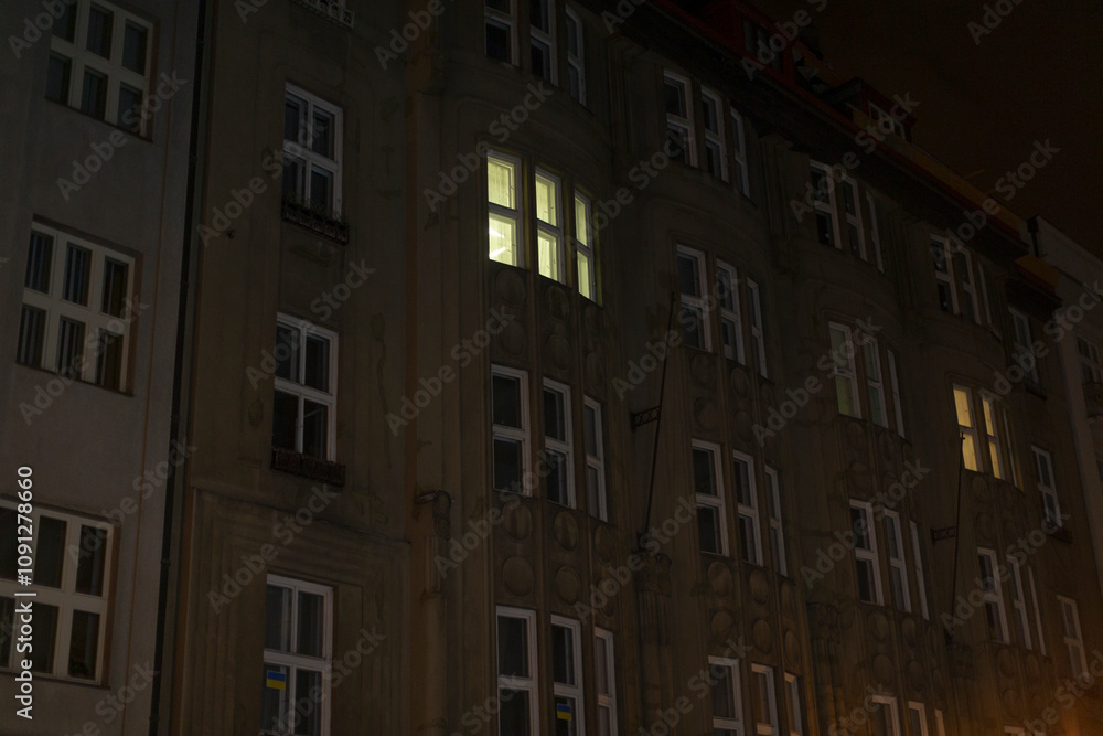 Fototapeta premium A captivating nighttime view showcases a residential building, where illuminated windows create a beautiful contrast and reflect the vibrant urban life that thrives in the city at night