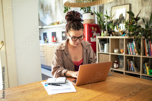 Young woman working from home on laptop with notes and paperwork photo