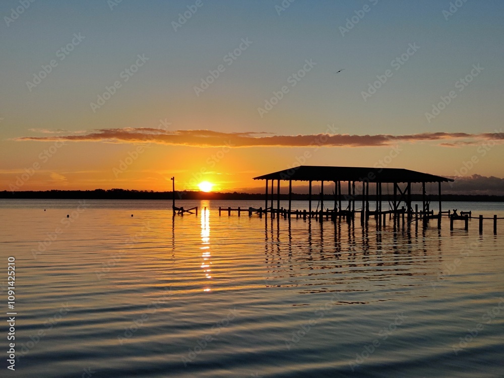 Obraz premium Sunset over tranquil lake and dock.