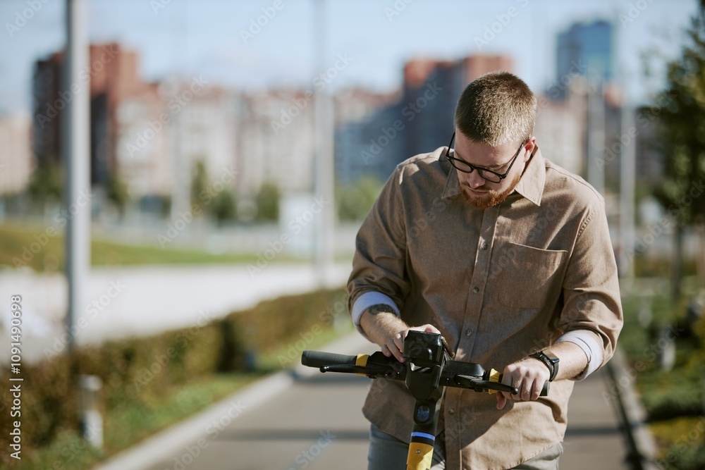 Fototapeta premium Man riding electric scooter on pathway within urban area, focusing on handlebar while background showcases blurred city buildings on sunny day