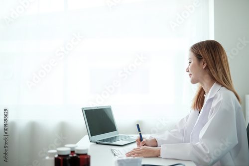 A woman is sitting at a desk with a laptop and a pen