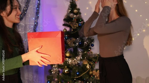 Friendship. Fun and laughter. New Year's atmosphere. Subdued cinematic light. Christmas tree and gifts. New Year's gift for a friend. Two girls celebrate the new year
