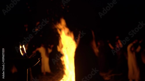 Unrecognizable people dance circle around a big campfire at night. Focus on the foreground 4K