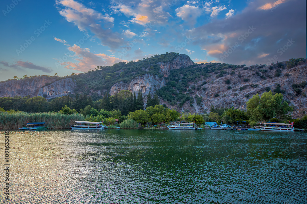 The rock-cut temple tombs of the ancient city of Kaunos in Dalyan, Muğla, Turkey. Beautiful view of Dalyan river with reed beds, excursion boats and carved tombs in the background.
