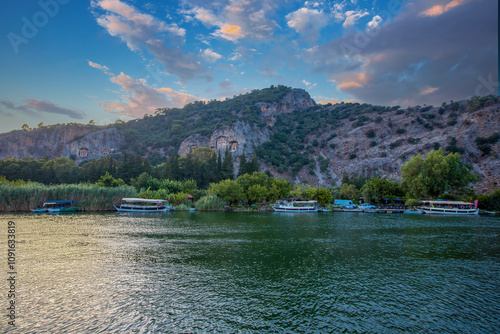Obraz na płótnie The rock-cut temple tombs of the ancient city of Kaunos in Dalyan, Muğla, Turkey. Beautiful view of Dalyan river with reed beds, excursion boats and carved tombs in the background. w salonie