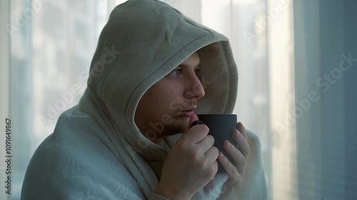 A man with a bitter drink is standing outside the window.
A man in a warm blanket drinks hot tea at home.
A man warms himself under a blanket in winter.
Cold in the apartment and a man in a blanket photo