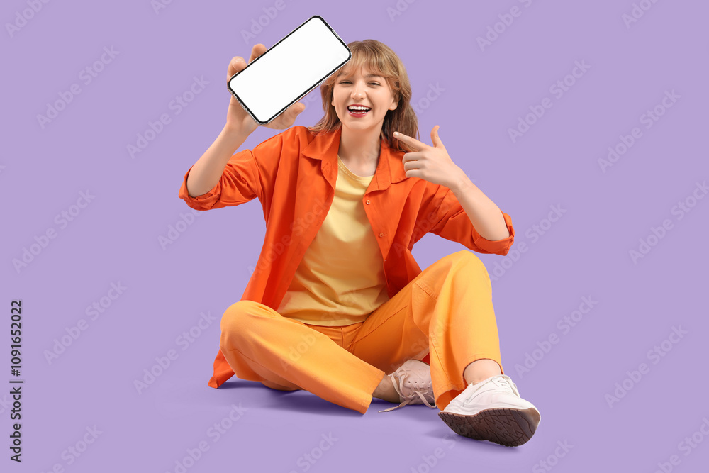 Fashionable young woman pointing at mobile phone with blank screen on purple background Fashionable young woman pointing at mobile phone with blank screen on purple background
