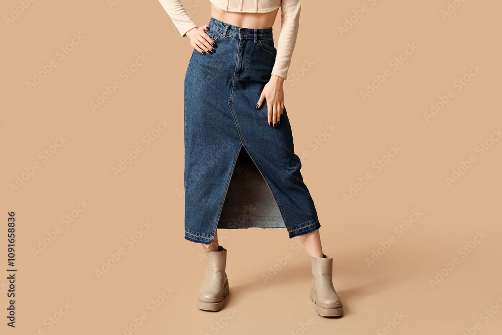 Naklejka premium Legs of beautiful young woman wearing blue long denim skirt on beige background
