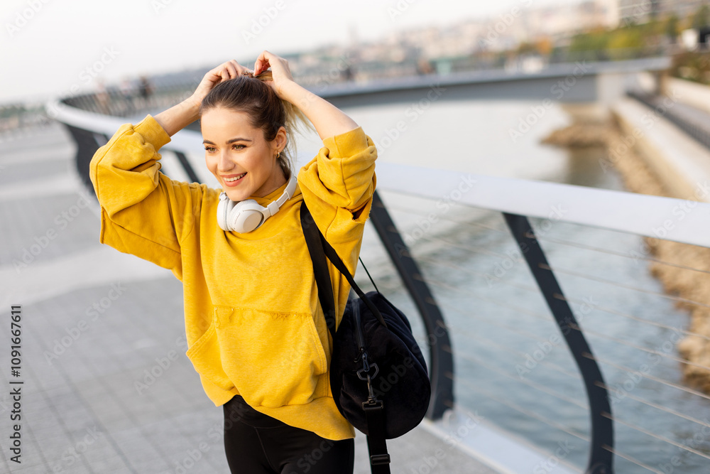 Obraz premium Joyful woman strolls along a riverside promenade in a vibrant yellow hoodie, enjoying the evening breeze and the soft sunset glow