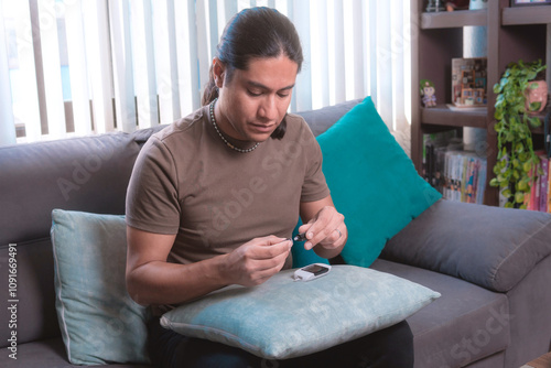 Middle-aged man measures his blood sugar level with a glucometer, he is sitting on the couch at home, home health.