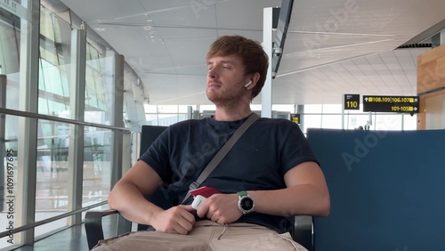 handsome young man looking at phone in airplane waiting area with tickets, travel, flight, alone