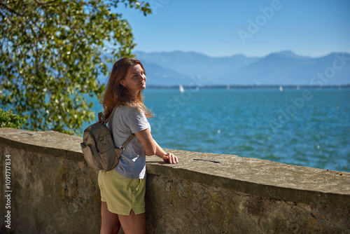 Stunning Woman with Backpack Enjoying Scenic Views of Bodensee and the Alps on a Sunny Day. Idyllic Lakeside Setting Captures the Essence of Outdoor Adventure and Natural Beauty in Europe.
