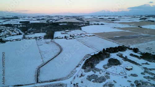 Aerial view over snow covered farmlands and villages in Aberdeenshire, Scotland. Sunrise lighting gives pink clear skies over white wintery landscape.  photo