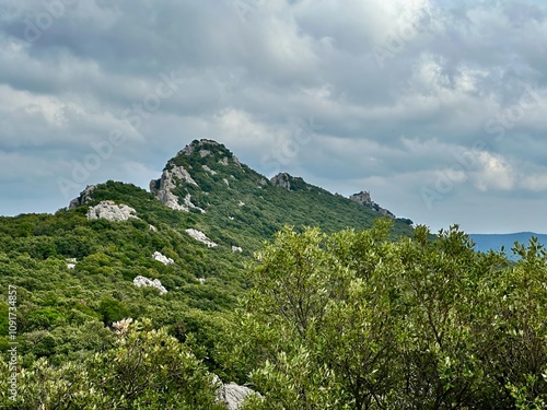 View of Col de la Pousterle and Château de Montferrand Among Lush Mediterranean Forest and Limestone Peaks Under a Dramatic Clouded Sky Near Pic Saint-Loup, Southern France