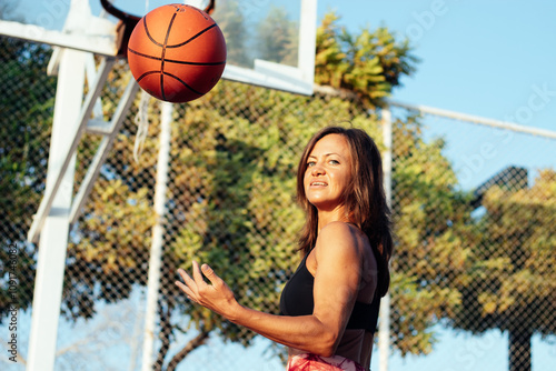 Woman tosses ball and looks at camera on basketball court photo