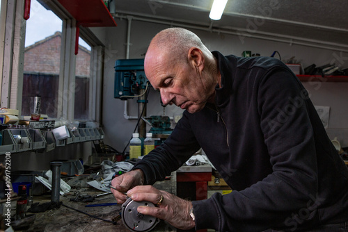 A mature retired man restoring a vintage motorbike in his garden shed workshop.
