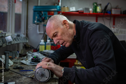 A mature retired man restoring a vintage motorbike in his garden shed workshop.