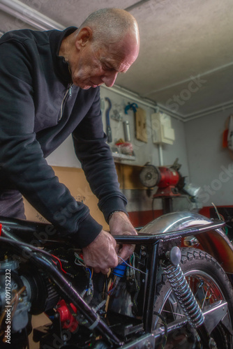 A mature retired man restoring a vintage motorbike in his garden shed workshop.