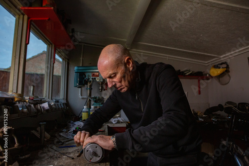 A mature retired man restoring a vintage motorbike in his garden shed workshop.