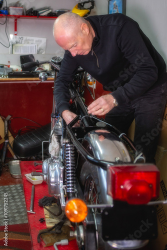 A mature retired man restoring a vintage motorbike in his garden shed workshop.