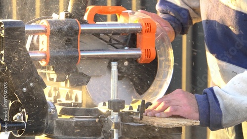 A man works with a construction tool. Table saw for wood. In the background is a house. Outdoors. Construction work. Tool. Close-up.