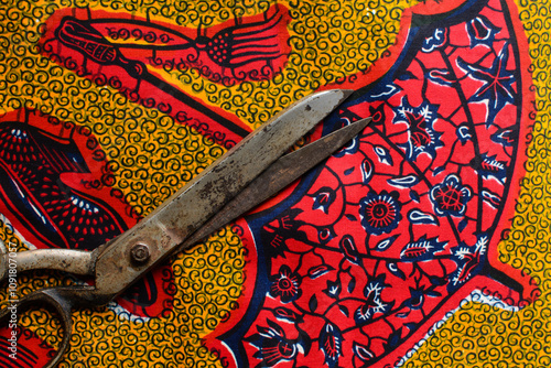 Top view of tarnished silver scissors on red yellow ankara fabric, large antique tailor scissors and ankara material on a table photo