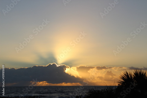 sunrise over ocean with sun rays peeking through clouds 