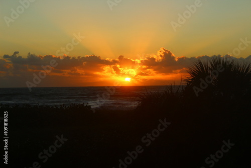 sunrise on beach over ocean with sun rays bursting through the clouds