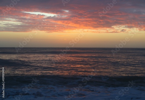 sunrise at the beach with pink clouds reflecting on the ocean waves