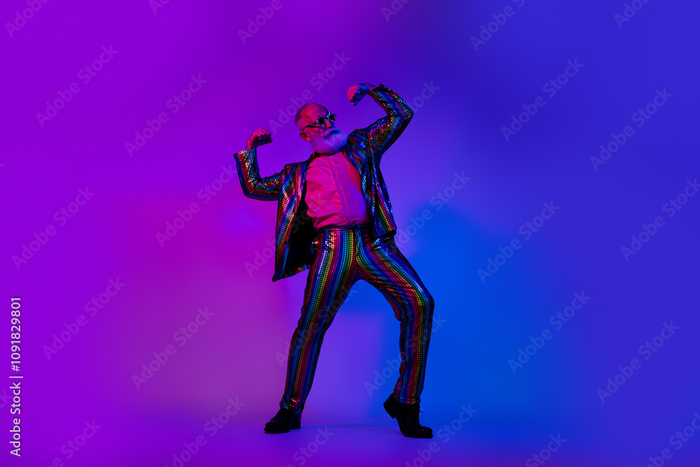 Full size photo of cool macho senior man show biceps dressed colorful sequins striped garment isolated on blue purple neon light background Full size photo of cool macho senior man show biceps dressed colorful sequins striped garment isolated on blue purple neon light background