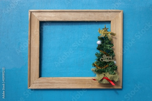 Empty wooden square frame with little Christmas tree on blue wooden background