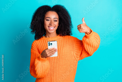 Photo portrait of attractive young woman hold device thumb up dressed stylish knitted orange clothes isolated on cyan color background photo