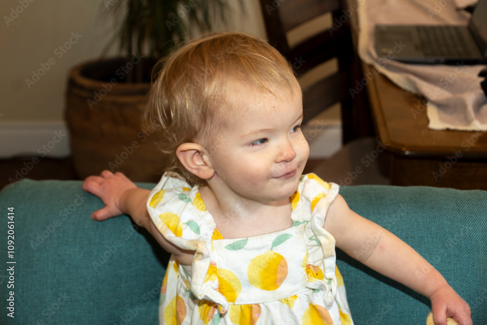 Little girl with a playful expression stands in a cozy living room filled with comfortable furniture Little girl with a playful expression stands in a cozy living room filled with comfortable furniture