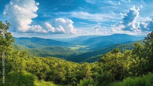 Panoramic view of a lush green valley surrounded by mountains under a blue sky with white clouds.