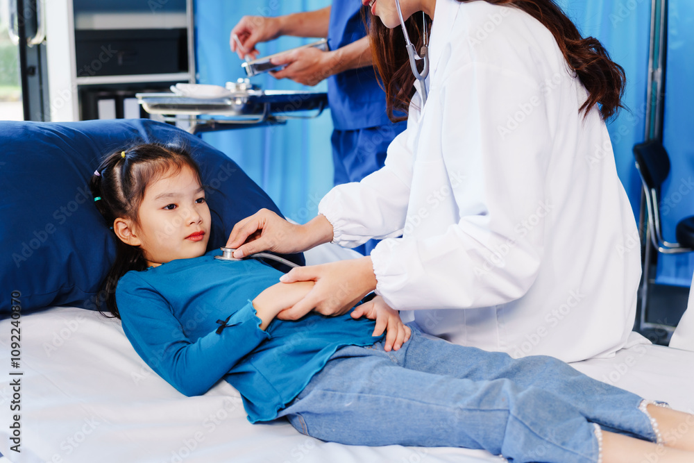 Fototapeta premium A doctor listens to a little girl’s heartbeat with a stethoscope while she lies on a bed in the hospital. The doctor is conducting a routine checkup to monitor her health