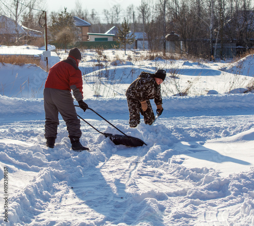 Two men are shoveling snow from a driveway photo