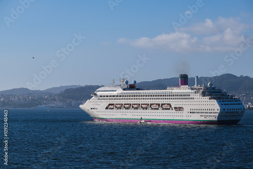 Classic cruiseship cruise ship liner Ambience sail away departure from Vigo port, Spain in Galicia during summer Atlantic Coast cruising with blue sky and coast line