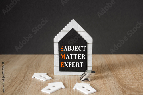 Concept words SME, subject matter expert on black blackboard. Beautiful wooden table, black background. A stack of coins. Business, SME, subject matter expert concept.