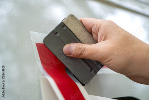 A person installing foil stickers on a car. Applying the sticker with a plastic spatula.